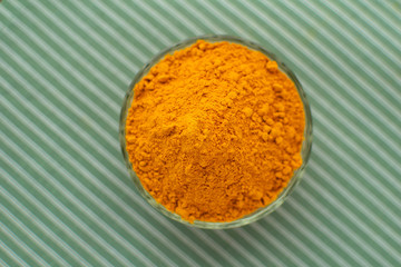 Top view at turmeric powder in glass bowl at green background. Healthy food. Indian spices.