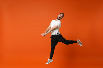 Fototapeta na wymiar Cheerful crazy young man in casual white t-shirt posing isolated on bright orange wall background studio portrait. People lifestyle concept. Mock up copy space. Having fun, fooling around, jumping.