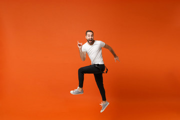 Excited crazy young man in casual white t-shirt posing isolated on bright orange wall background studio portrait. People lifestyle concept. Mock up copy space. Having fun, fooling around, jumping.