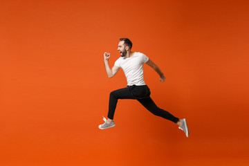 Fototapeta na wymiar Side view of crazy young man in casual white t-shirt posing isolated on bright orange wall background studio portrait. People lifestyle concept. Mock up copy space. Having fun fooling around, jumping.