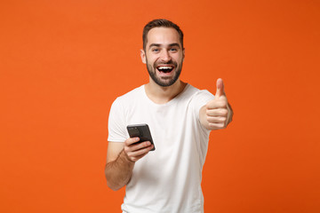 Cheerful young man in casual white t-shirt posing isolated on orange wall background in studio....