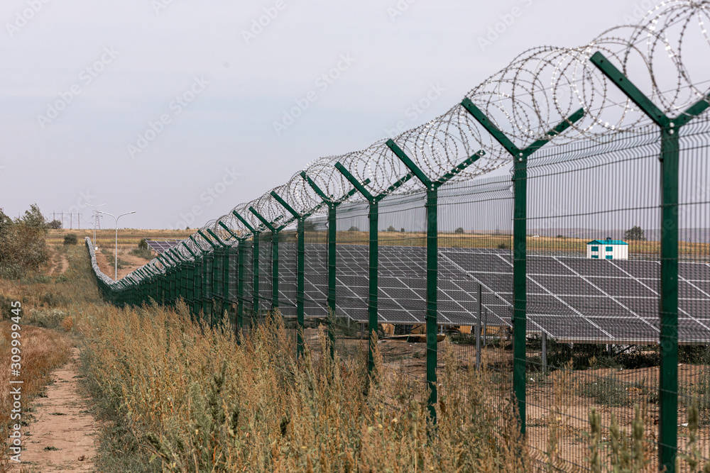 Wall mural solar power station protected from road by barbed wire fence. fencing of sensitive sites with barbed