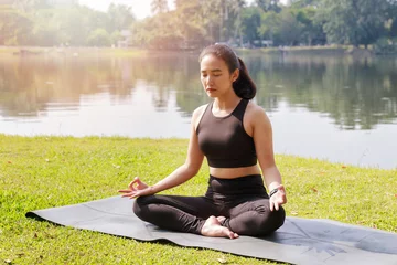  Asian woman practicing yoga in lotus position in outdoor park. © skarie