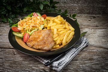 Fried pork chop in breadcrumbs, served with fries and salad.