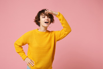 Curious young brunette woman girl in yellow sweater posing isolated on pastel pink background in...