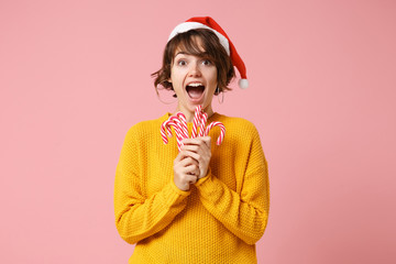 Shocked young brunette woman Santa girl in yellow sweater Christmas hat posing isolated on pink...