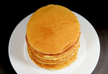 Closeup stack of fresh made pancakes on white plate on black background