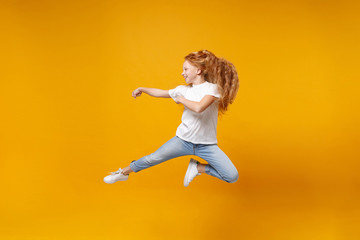 Side view of little ginger kid girl 12-13 years old in white t-shirt isolated on yellow background children portrait. Childhood lifestyle concept. Mock up copy space. Having fun, fooling around, jump.