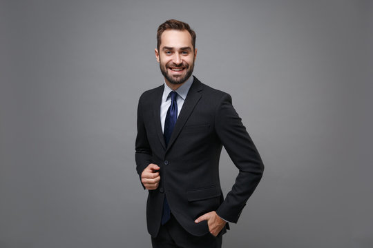 Smiling young bearded business man in classic black suit shirt tie posing isolated on grey background studio portrait. Achievement career wealth business concept. Mock up copy space. Looking camera.