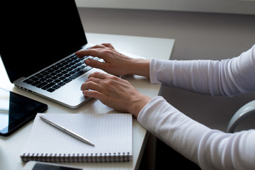 Horizontal view image of woman's hands using and typing on laptop with coffee cup, notebook, tablet in white colors on table. Business woman, feminine, business background