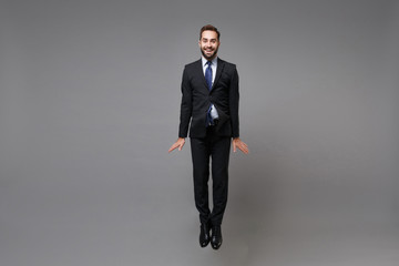 Smiling young business man in classic black suit shirt tie posing isolated on grey wall background....