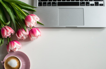 Home office desk in pink colors with laptop, cup of coffee, rose notebook, phone, pink tulips on a...