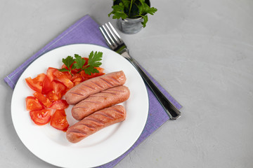Breakfast of sausages and vegetables. Tomato sliced. On a light background.