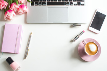 Home office desk in pink colors with laptop, cup of coffee, rose notebook, phone, pink tulips on a white background. Flat lay Business womans workplace and objects. Top view. Copy space for text