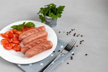 Breakfast of sausages and vegetables. Tomato sliced. On a light background.
