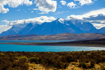 Under a blue, partially clouded sky, you can see the famous 'Torres del Paine'. These mountain peaks are the destination of a stunning trekking circuit. In the foreground lies Lake Sarmiento.