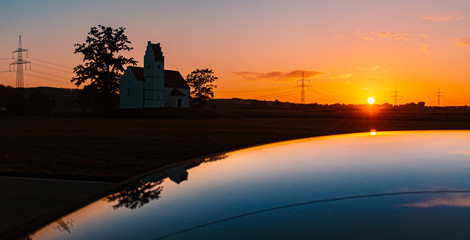 Beautiful sunset with a church and reflections on a car roof near Huett, Bavaria, Germany