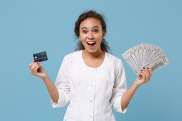 Excited african american doctor woman isolated on blue background. Female doctor in medical gown hold fan of cash dollar money, credit card. Healthcare personnel medicine concept. Mock up copy space.