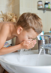 baby boy washing his face in bathroom over sink