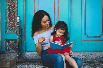 Young Asian woman sitting with daughter and teaching to read