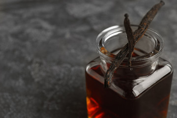 Aromatic homemade vanilla extract and dry pods on grey table, closeup. Space for text
