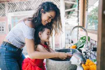 Curly woman with little girl washing hands in sink