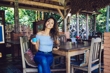 Beautiful curly woman holding phone and cup in hand