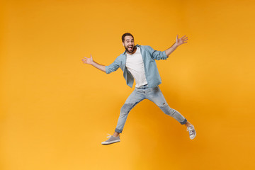 Fototapeta na wymiar Excited young bearded man in casual blue shirt posing isolated on yellow orange wall background studio portrait. People emotions lifestyle concept. Mock up copy space. Jumping, spreading hands, legs.