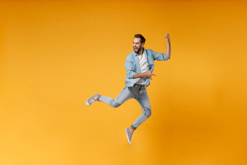 Fototapeta na wymiar Funny young bearded man in casual blue shirt posing isolated on yellow orange wall background studio portrait. People lifestyle concept. Mock up copy space. Jumping fooling around like playing guitar.