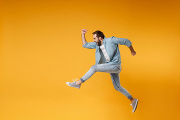 Fototapeta na wymiar Side view of crazy young bearded man in casual blue shirt posing isolated on yellow orange background studio portrait. People sincere emotions lifestyle concept. Mock up copy space. Jumping, running.