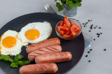 Breakfast of sausages and fried eggs. Tomato sliced. On a light background.