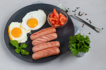 Breakfast of sausages and fried eggs. Tomato sliced. On a light background.