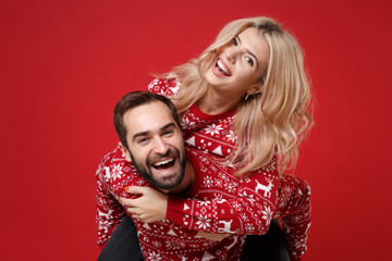 Laughing young couple guy girl in Christmas sweaters posing isolated on red background. Happy New...