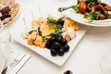 Cheese, grapes and honey on the table. Delicious dishes on the table in the restaurant. Sliced cheese with honey on a white plate. Cheese. Food. Festive table with dishes. Dish.