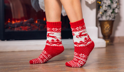 Legs young girl in red golf on socks walks after Christmas gifts on background of fireplace