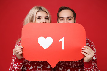Young couple guy girl in Christmas sweaters posing isolated on red background. New Year 2020...