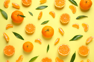 Flat lay composition with fresh ripe tangerines and leaves on light yellow background. Citrus fruit
