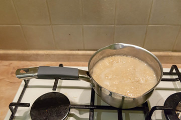 Oatmeal porridge cook in a metal silver saucepan on a gas stove.