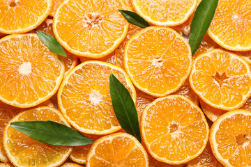 Slices of fresh ripe tangerines and leaves as background, top view. Citrus fruit