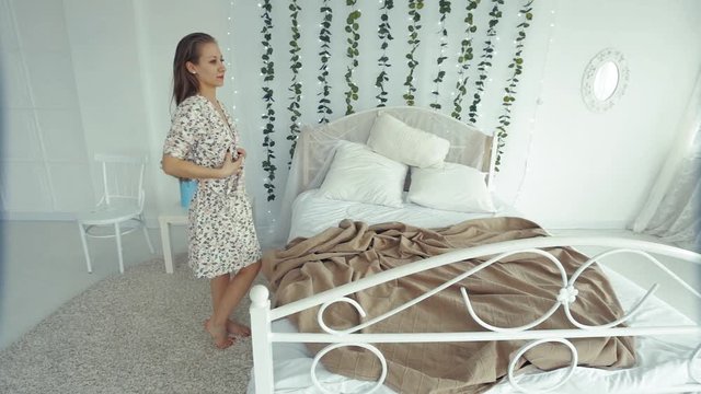 the girl takes off her white silk robe. The girl drops the robe from her shoulders on the bed
