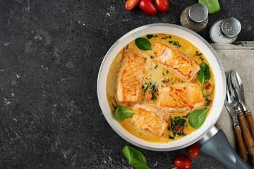 Delicious salmon steaks in cream sauce on black background