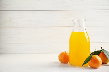 Fresh tangerines and bottle of juice on white wooden table. Space for text