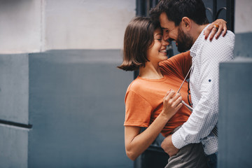 Beautiful young caucasian couple on a romantic date, hugging with passion and touching heads by the building entrance.