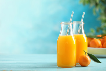 Fototapeta premium Bottles of fresh tangerine juice on blue wooden background. Space for text