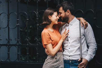 Young beautiful Caucasian couple, smiling, embracing with passion and cuddling by the iron fence.