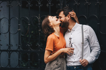 Young attractive Caucasian couple embracing, laughing and enjoying their romantic date while standing by the iron fence.