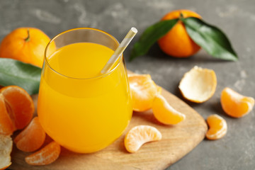 Fresh tangerines and glass of juice on grey table