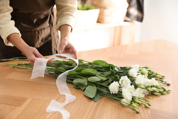 Florist making beautiful bouquet at table in workshop, closeup