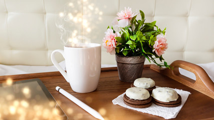 Wooden table, tray, white cup of coffee, flowers on the table, tablet. Sunlight, ray. Abstract bokeh light.