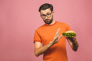 Handsome young man refusing unhealthy burger isolated over pink background. Diet concept. With copy...